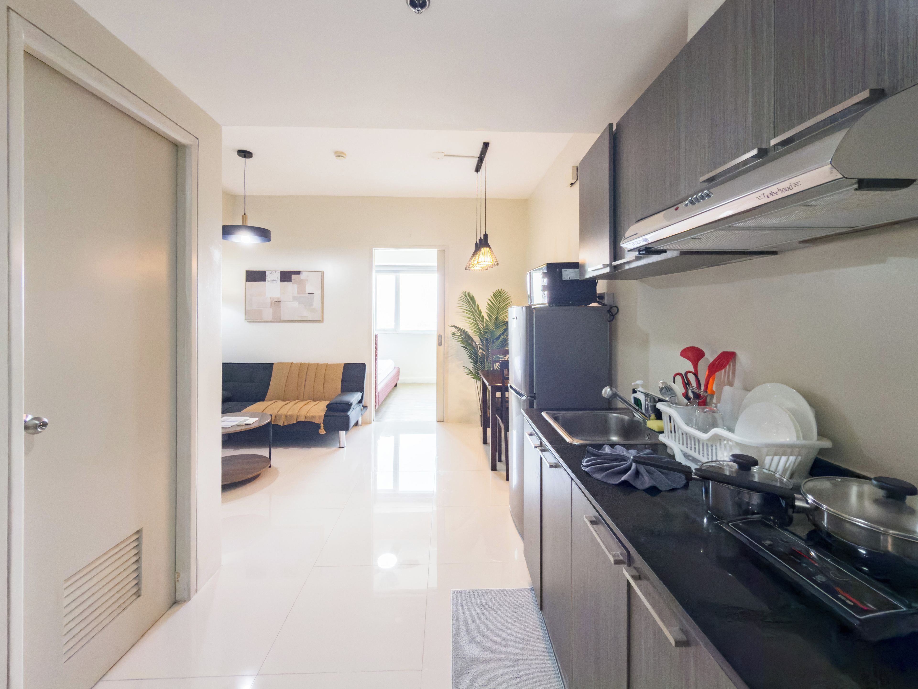 A modern kitchen with a built-in stove, a sink, and a refrigerator. There is a dining area with a sofa and a table in the background.