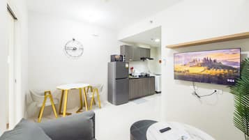 Un espacio habitable compacto con kitchenette, una zona de comedor y una sala de estar con un televisor montado en la pared.