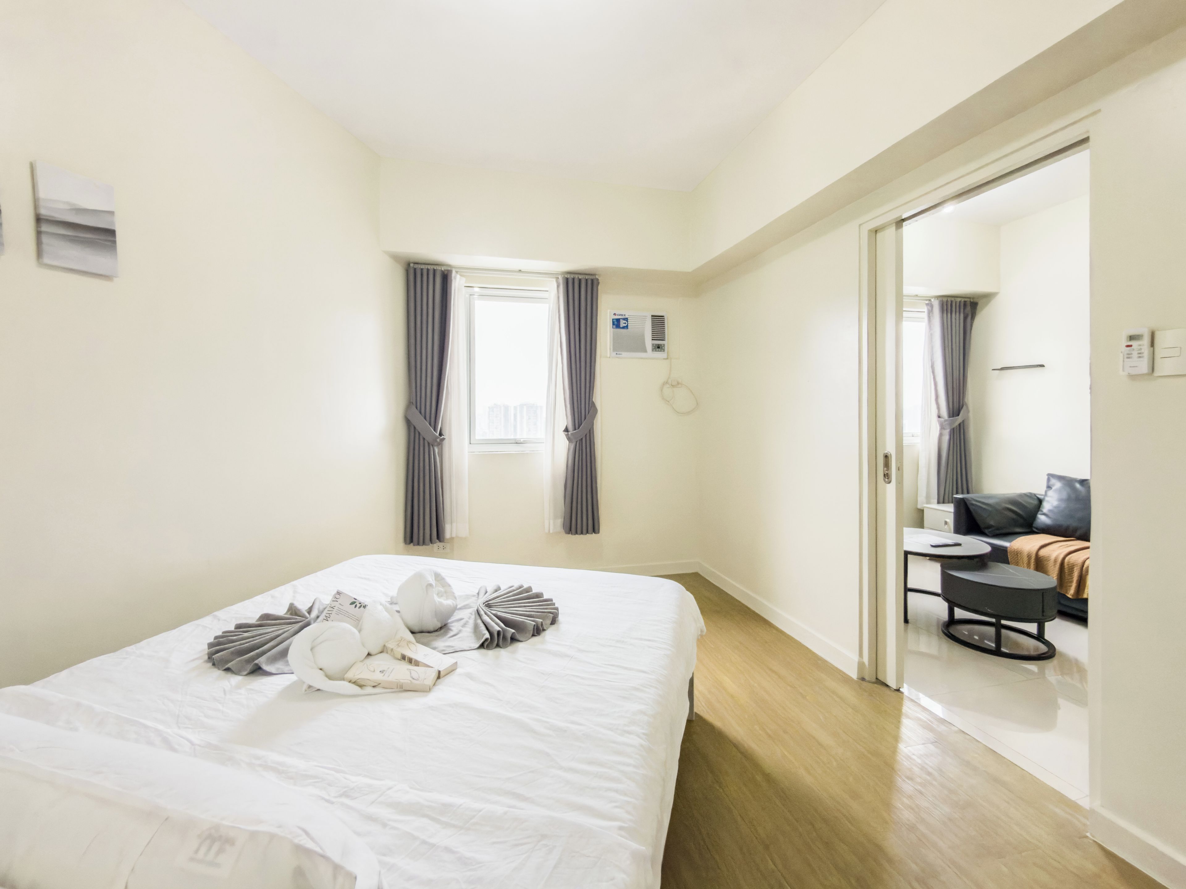A hotel room with a large bed, a small table, a sofa, and a view of the city through the window.