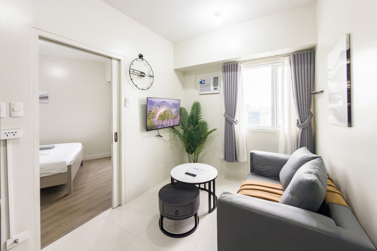 Una sala de estar moderna con un sofá, una mesita, una planta en maceta y un televisor en la pared.