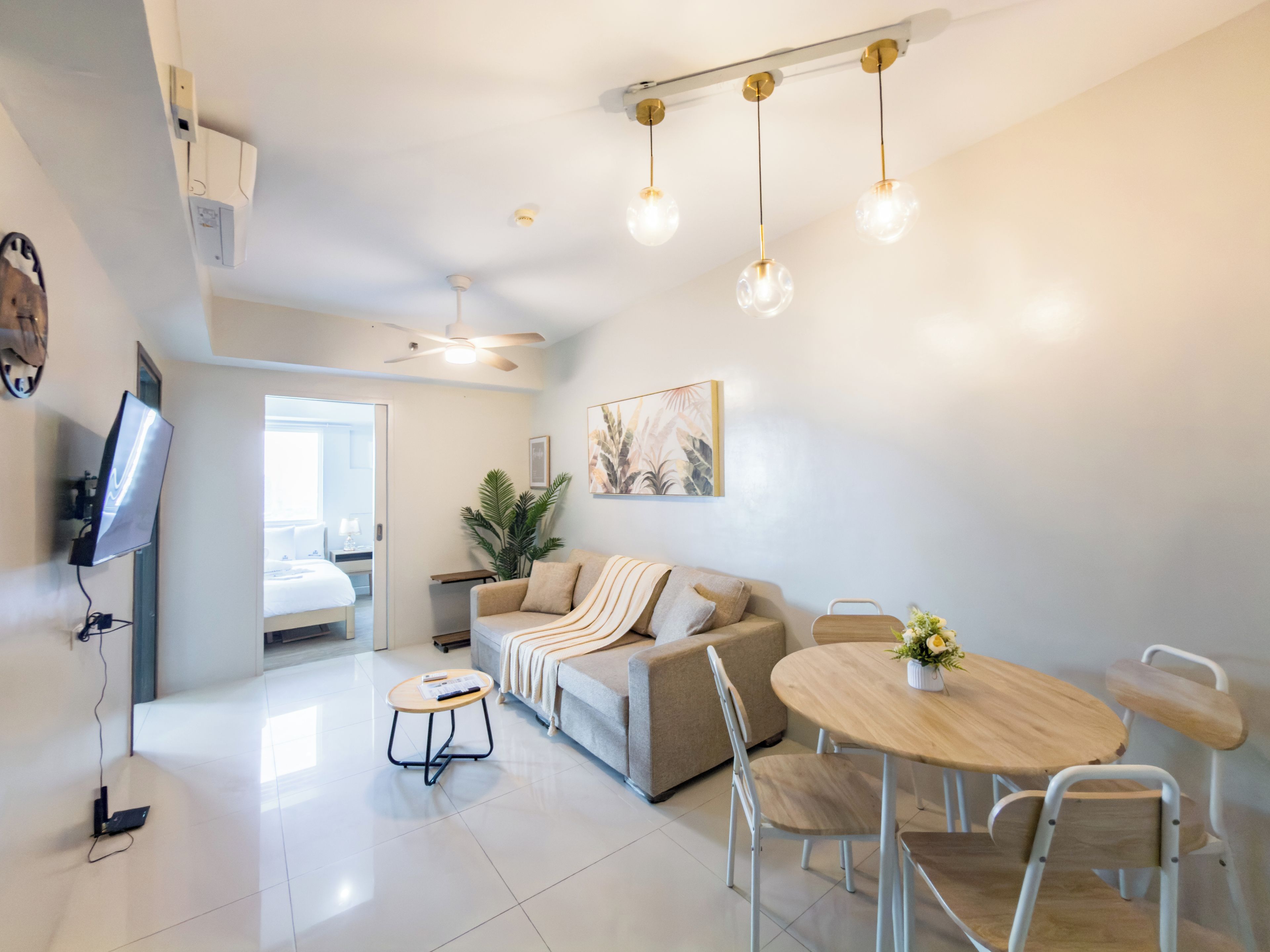 A modern living room with a sofa, a dining table, and a TV mounted on the wall.