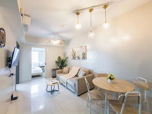 A modern living room with a sofa, a dining table, and a TV mounted on the wall.