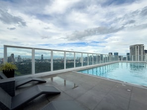 Une piscine sur le toit offrant une vue sur la ville, entourée de rampes de verre et de chaises longues.