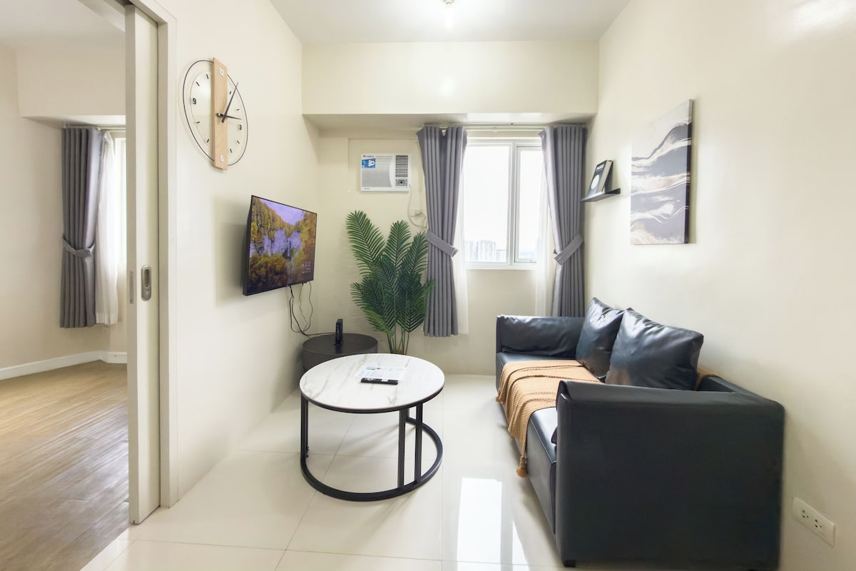 Una sala de estar moderna con un sofá, una mesa de centro, un televisor de pantalla plana, un reloj y una planta.