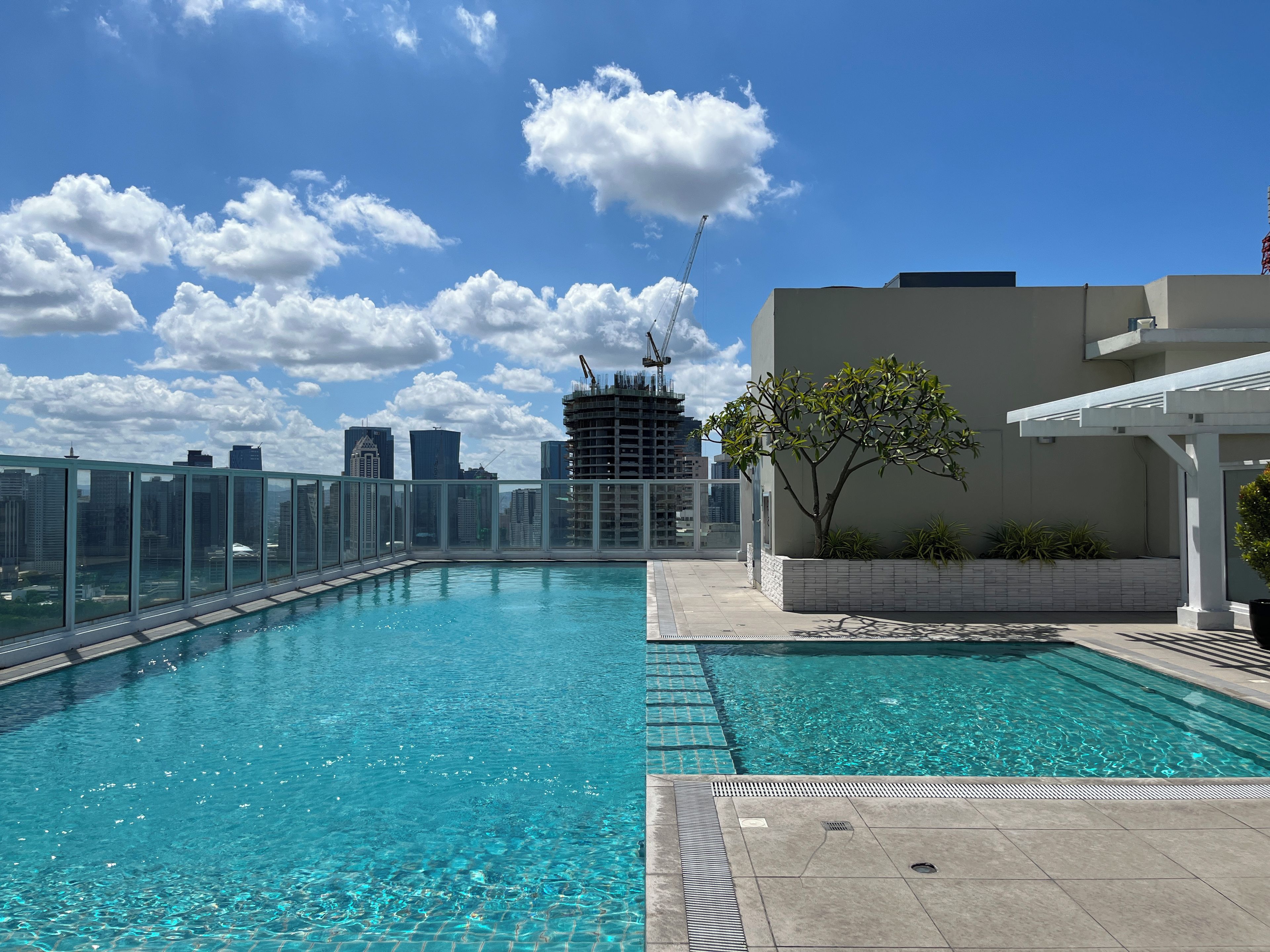 A rooftop swimming pool with clear blue water, surrounded by a glass barrier and a white building.