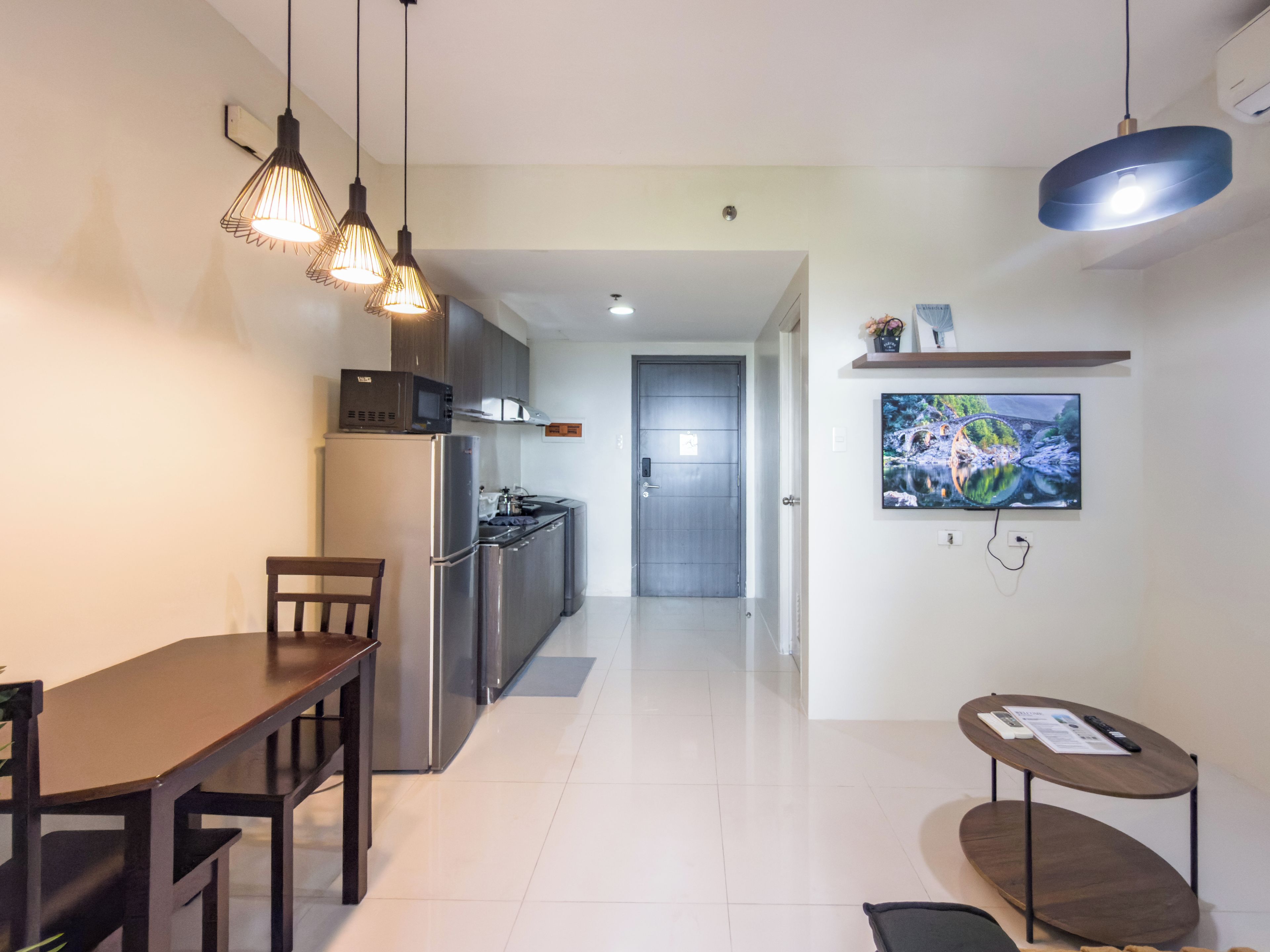 Una cocina moderna con electrodomésticos de acero inoxidable, un comedor con mesa de madera y un televisor montado en la pared.