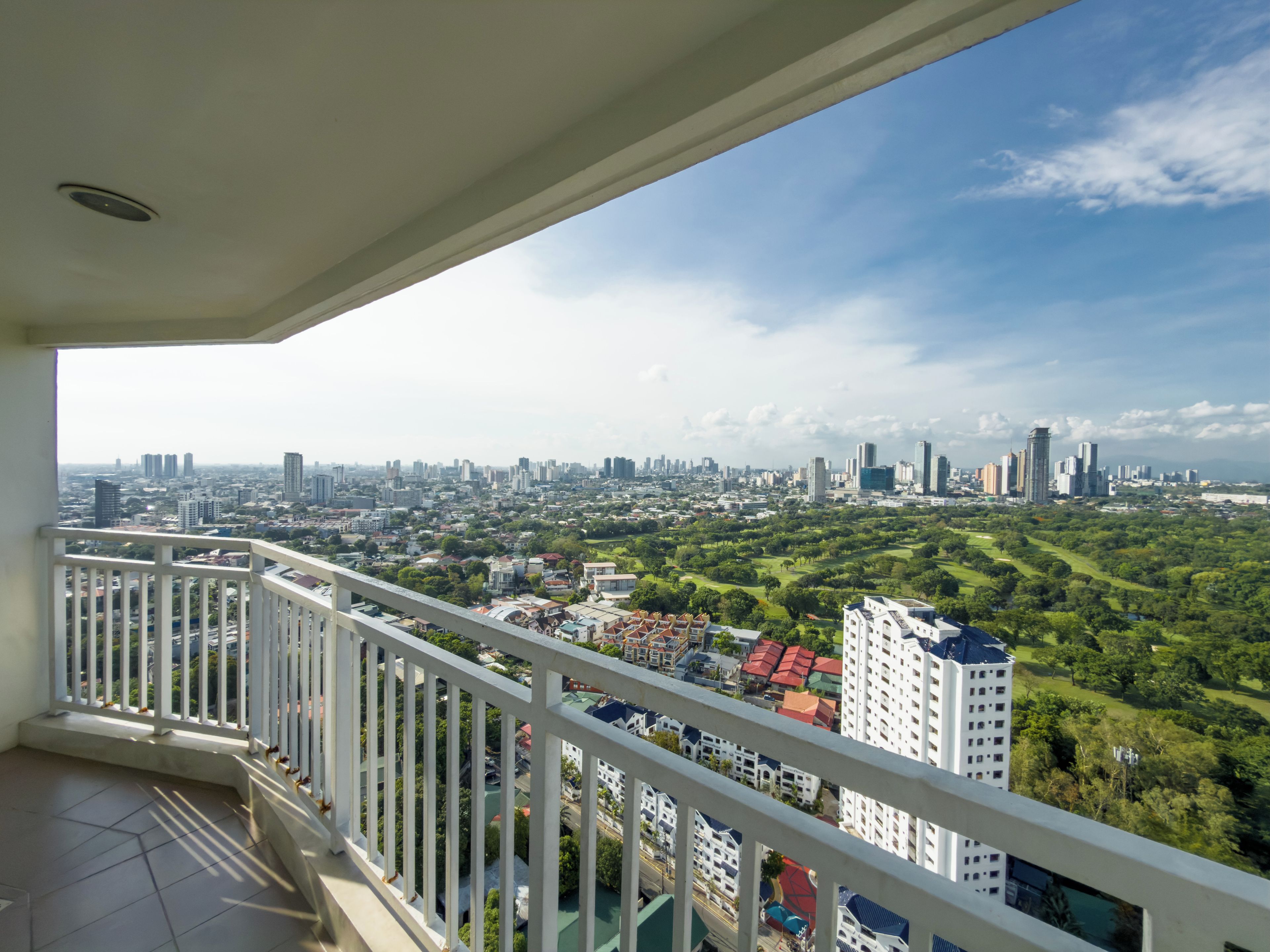A balcony with a city view, including high-rise buildings and greenery.