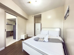 Un dormitorio con cama, mesitas de noche, un armario y una puerta que da a otra habitación.