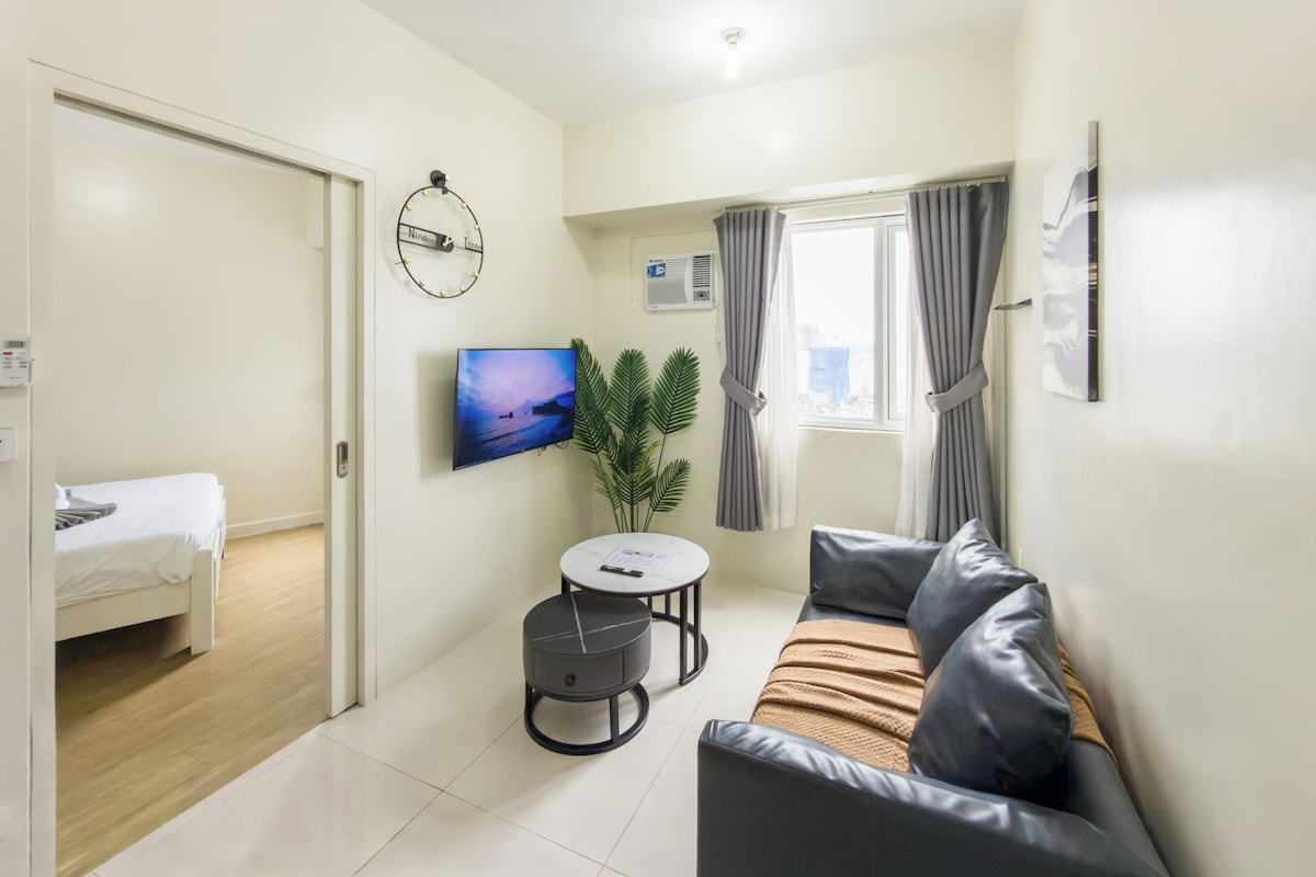 Una sala moderna con un sofá, una mesita redonda, un televisor y una planta en maceta.