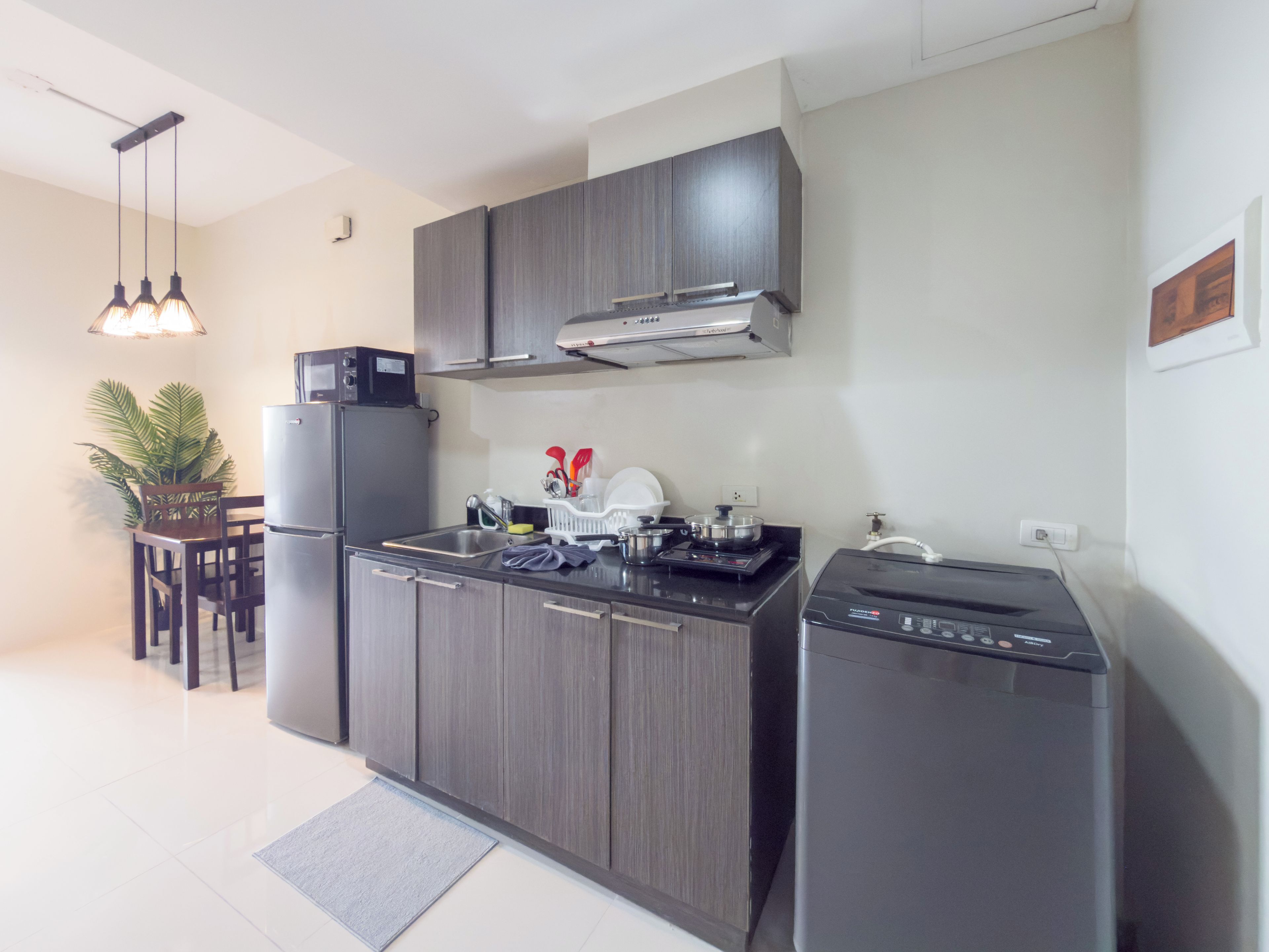 Una cocina moderna con horno empotrado, refrigerador y lavavajillas. Hay una mesa de comedor con sillas y una planta en maceta.