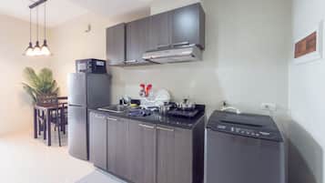 Una cocina moderna con horno empotrado, refrigerador y lavavajillas. Hay una mesa de comedor con sillas y una planta en maceta.