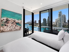 A modern hotel room with a large bed, a city view, and a painting of a beach scene. - Luxury Chevron Island Retreat Water & City Views (Gold Coast)