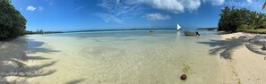 Una platja amb aigua turquesa cristal·lina, sorra daurada i un veler.