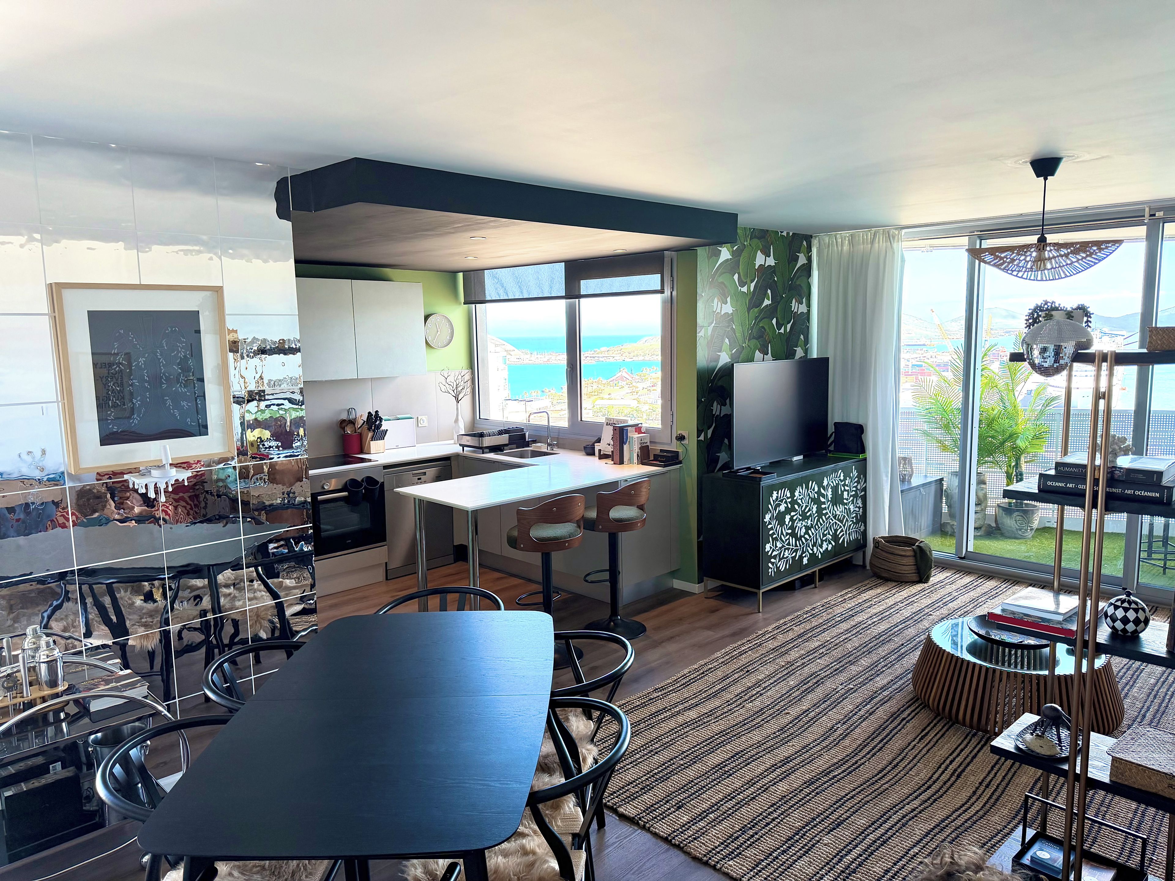 A modern kitchen with a dining area, large windows, and a view of the sea.