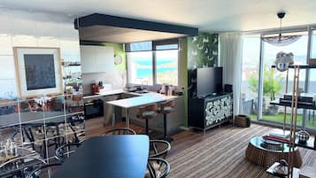 A modern kitchen with a dining area, large windows, and a view of the sea.
