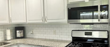 A kitchen with white cabinets, a granite countertop, a stainless steel stove, and a microwave.