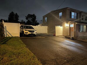Eine Auffahrt zu einem Wohnhaus mit einem weißen SUV am Eingang, einem Holzzaun und einem Haus mit sichtbarer Garagentür.