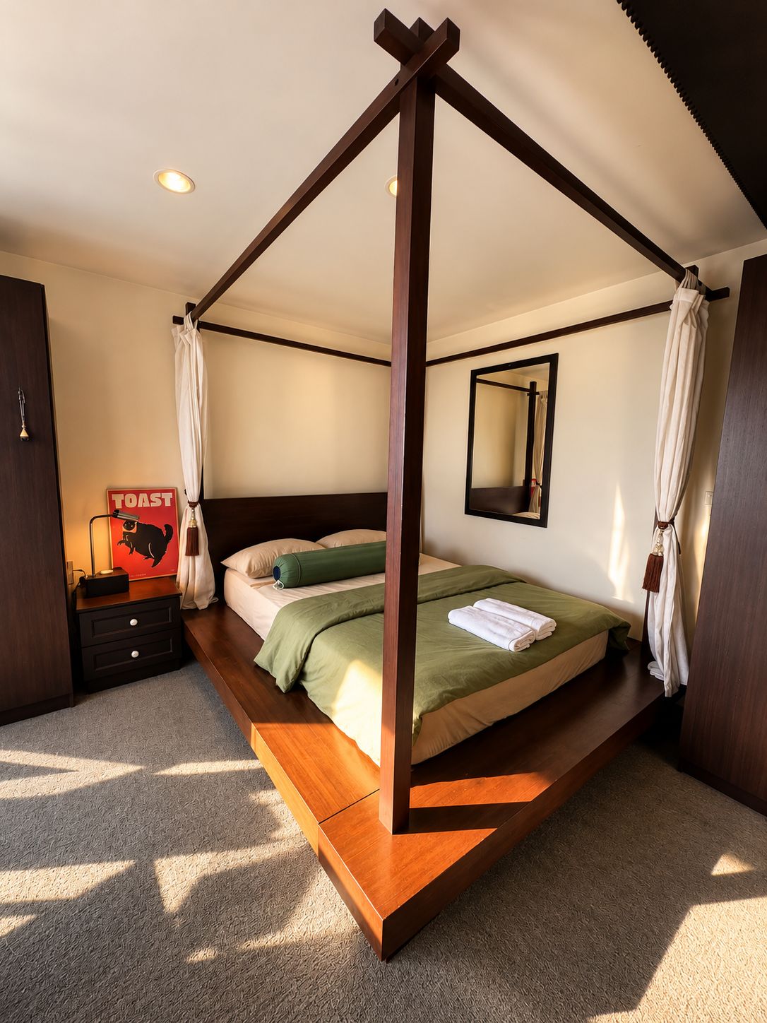A four-poster bed with a wooden frame, a bedside table with a lamp, and a sign on the wall.
