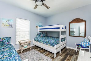 A bedroom with a bunk bed, a small table, a chair, a mirror, and artwork on the walls. - Make a Splash! 3BR with Pool & BBQ for 8 (Port Aransas)