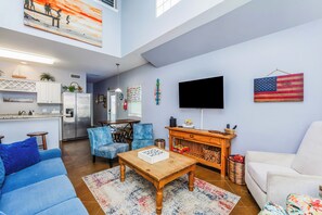 A spacious living room with a high ceiling, a kitchen area, and a dining space. - Make a Splash! 3BR with Pool & BBQ for 8 (Port Aransas)