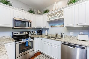 Cozinha moderna com armários brancos, eletrodomésticos de aço inoxidável, micro-ondas, fogão, cafeteira e máquina de lavar louça.