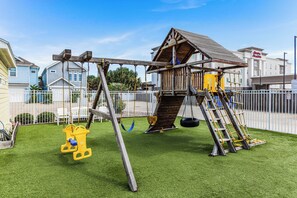 A playground with a wooden swing set, a climbing structure, and a tire swing. - Make a Splash! 3BR with Pool & BBQ for 8 (Port Aransas)