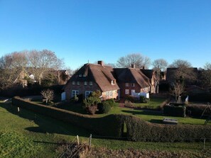 Ein traditionelles Backsteinhaus mit einem Reetdach, umgeben von einem gepflegten Rasen und Hecken.