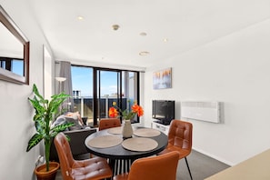 Un salon moderne avec une table ronde, des fauteuils en cuir, un téléviseur et une grande fenêtre donnant sur un beau paysage.