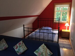 A bedroom with a sloped ceiling, a single bed with a metal frame, a nightstand with a lamp, and a window with a view of greenery. - Holiday Home in Eschede With Swimming Pool (Eschede)