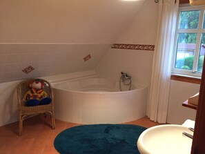 A bathroom with a bathtub, a wicker chair, a blue rug, and a window. - Holiday Home in Eschede With Swimming Pool (Eschede)