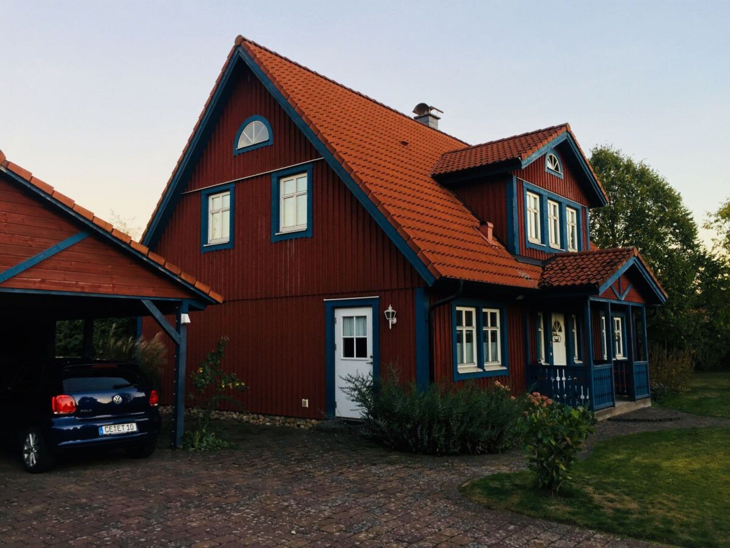 A two-story house with a red roof, a garage, and a car parked in front.