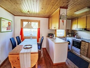 A compact kitchen with a dining area, wooden ceiling, and a window with curtains. - Yngvesväg 3 by Interhome (Bolmsö)