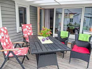 An outdoor patio with a table and chairs, a flower arrangement, and a sliding glass door leading to a covered area. - Yngvesväg 3 by Interhome (Bolmsö)