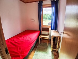 A small, single-bed room with a red bedspread, a wooden chair, and a small table. - Yngvesväg 3 by Interhome (Bolmsö)