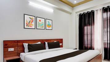 A bedroom with a wooden headboard, a bed with white and black bedding, and three framed artworks on the wall.