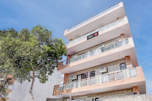 Un immeuble à plusieurs étages doté de balcons, une enseigne indiquant qu’il s’agit d’un hôtel, et un arbre au premier plan.