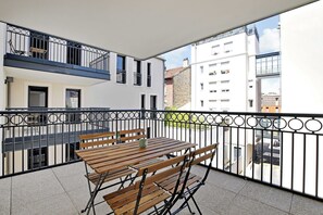 A balcony with a wooden table and benches, a metal railing, and a view of adjacent buildings. - Elegant Appt - 2bdr/6p - Near Paris & La Defense (Suresnes)