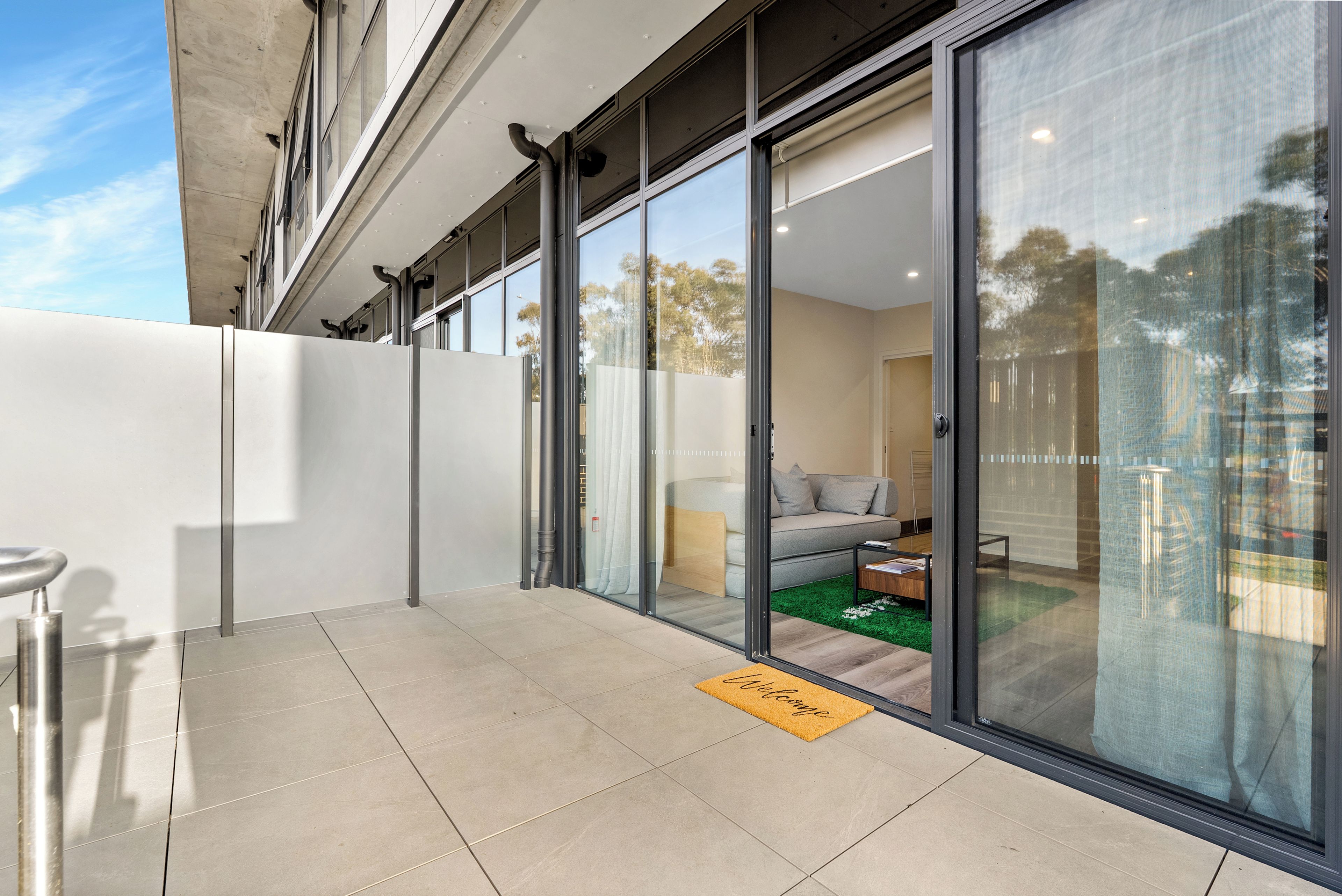 A modern building with a glass door entrance leading to a living area with a sofa and a coffee table.