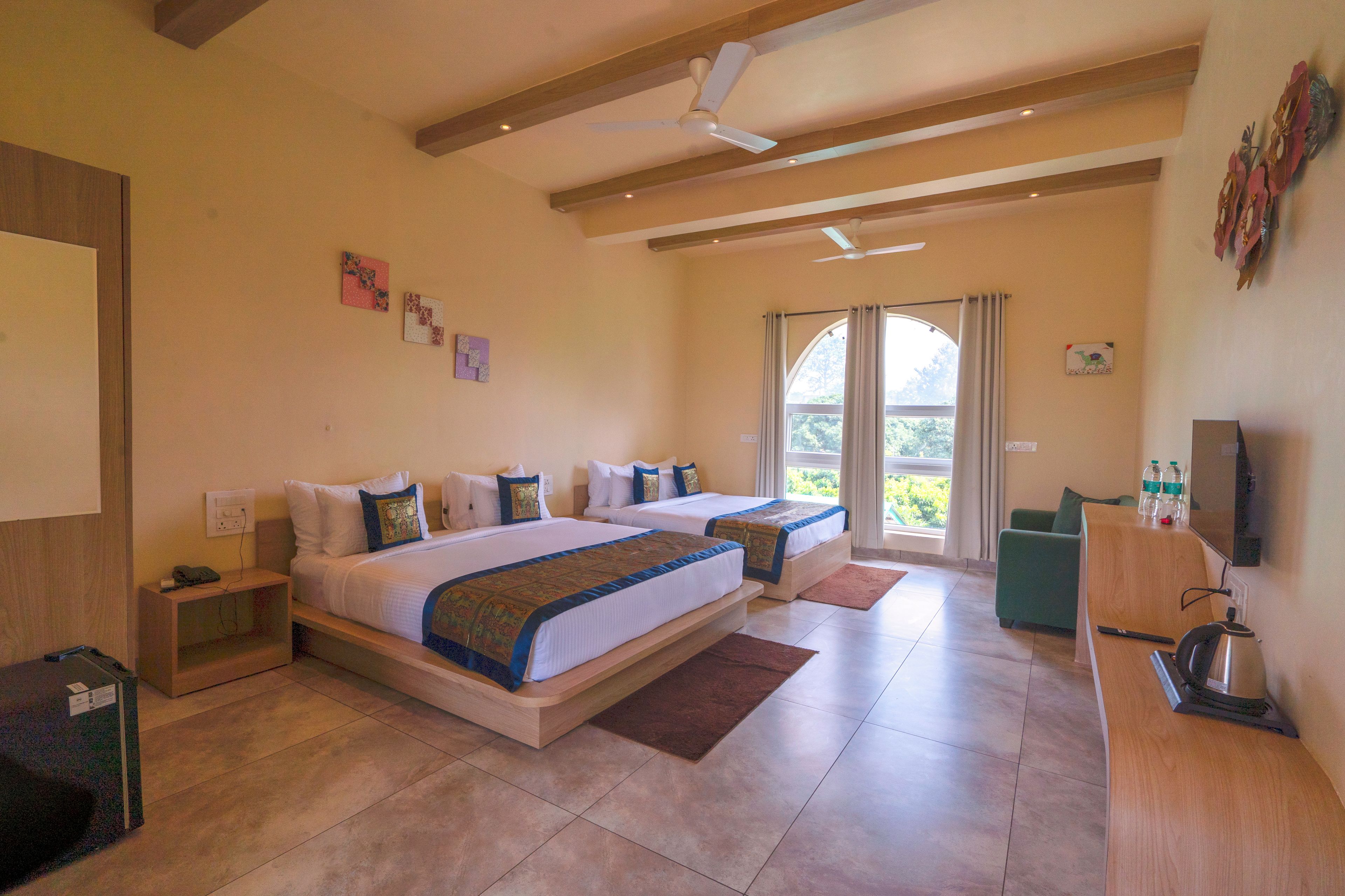 A hotel room with two beds, a desk, a chair, a coffee maker, and a window with curtains.