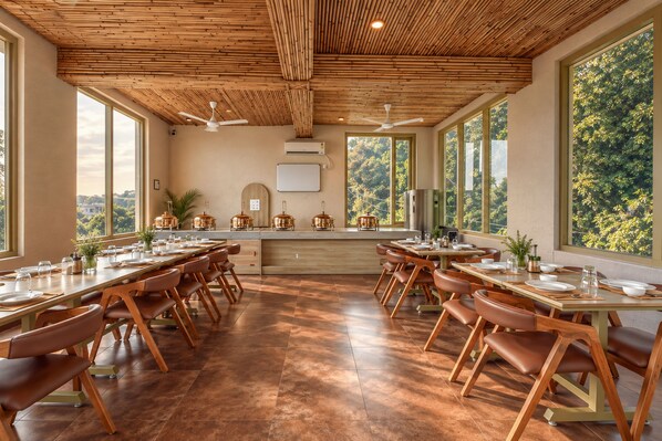 A spacious dining area with wooden tables and chairs, large windows, and a ceiling with a bamboo-like design.