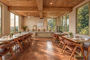 Un comedor amplio con mesas y sillas de madera, ventanas grandes y un techo con diseño que recuerda a la caña de bambú.
