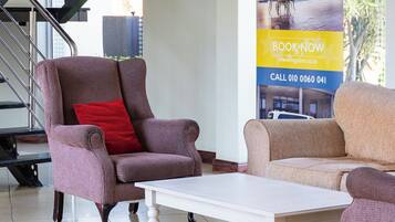 Un hall de hotel con una escalera, dos sillones, una mesa de centro blanca y un cartel promocional para Regal Inn.