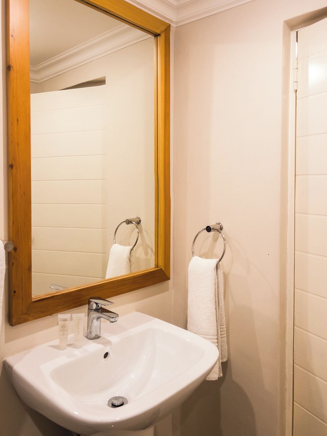 A bathroom with a white sink, a wooden-framed mirror, and a towel rack.