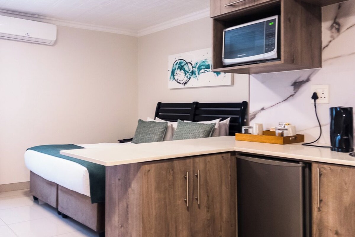 Una habitación compacta con cama, kitchenette equipada con microondas y cafetera.