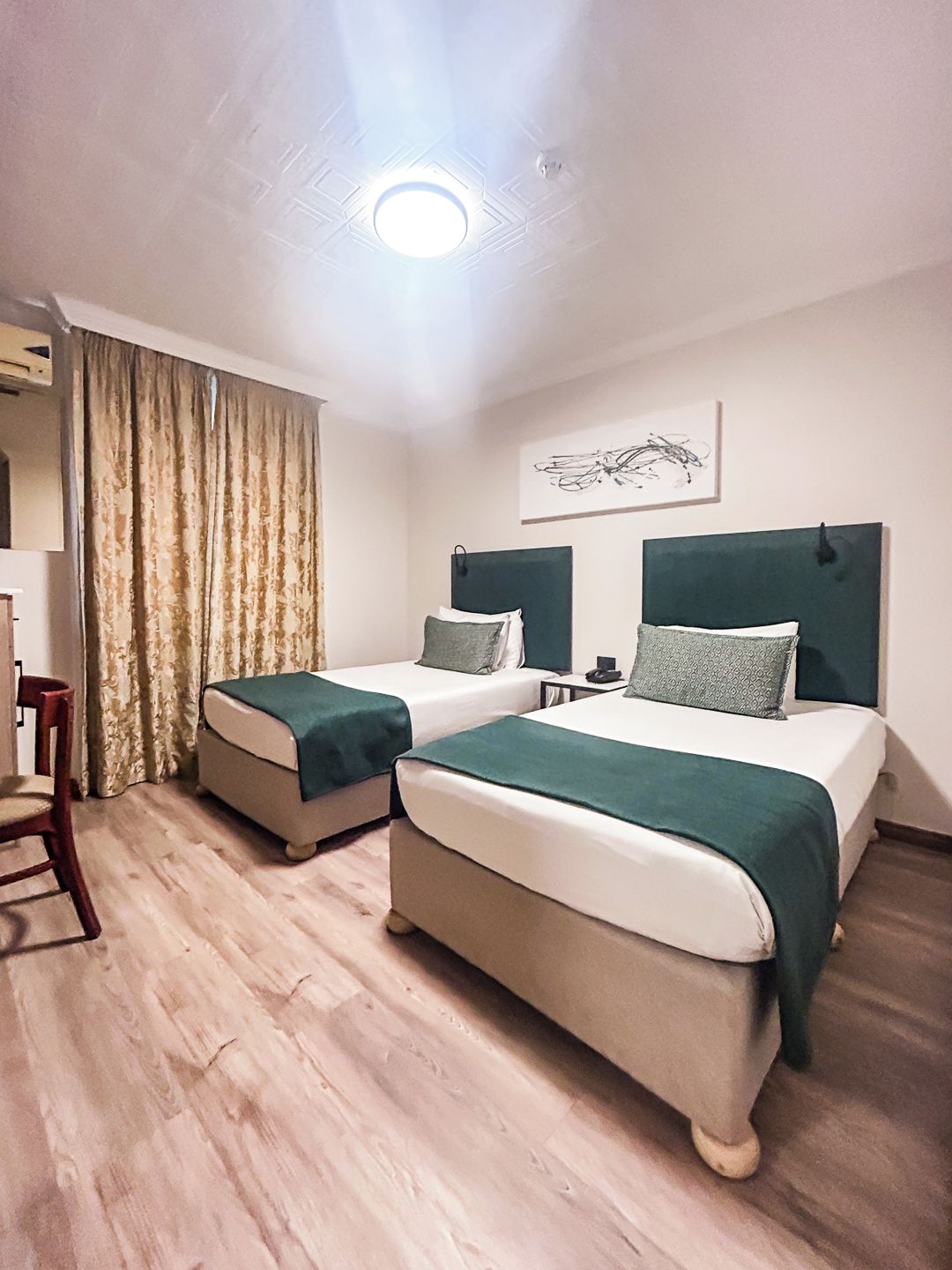 Une chambre d’hôtel avec deux lits, une chaise, un bureau et une fenêtre avec des rideaux.