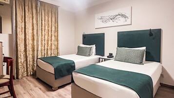 Une chambre d’hôtel avec deux lits, une chaise, un bureau et une fenêtre avec des rideaux.