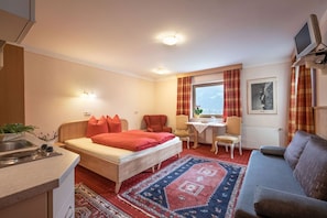 Et kompakt hotelværelse med seng, sofa, lille spisebord og tekøkken.