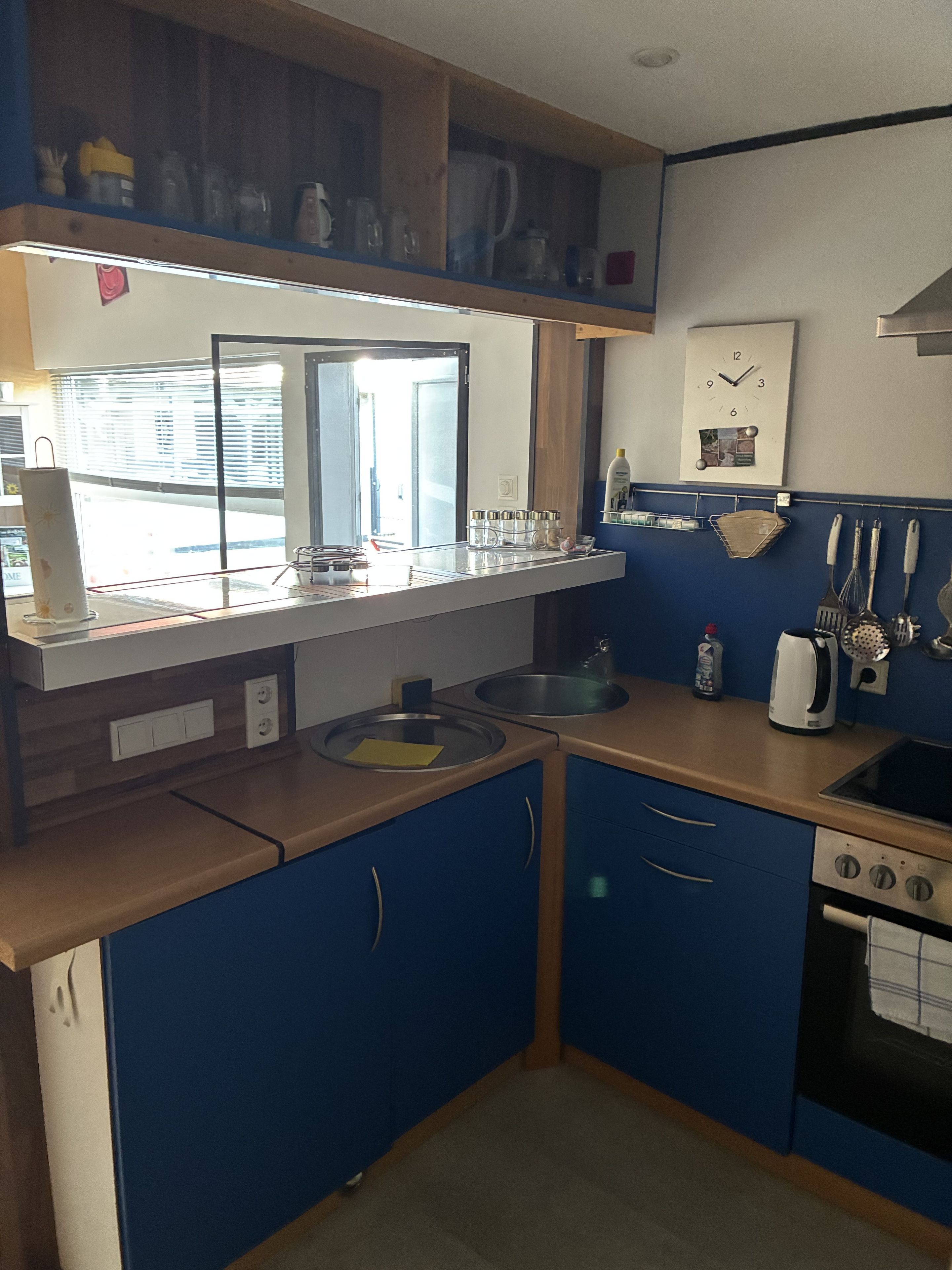 A compact kitchen with a sink, stove, and a window with blinds.