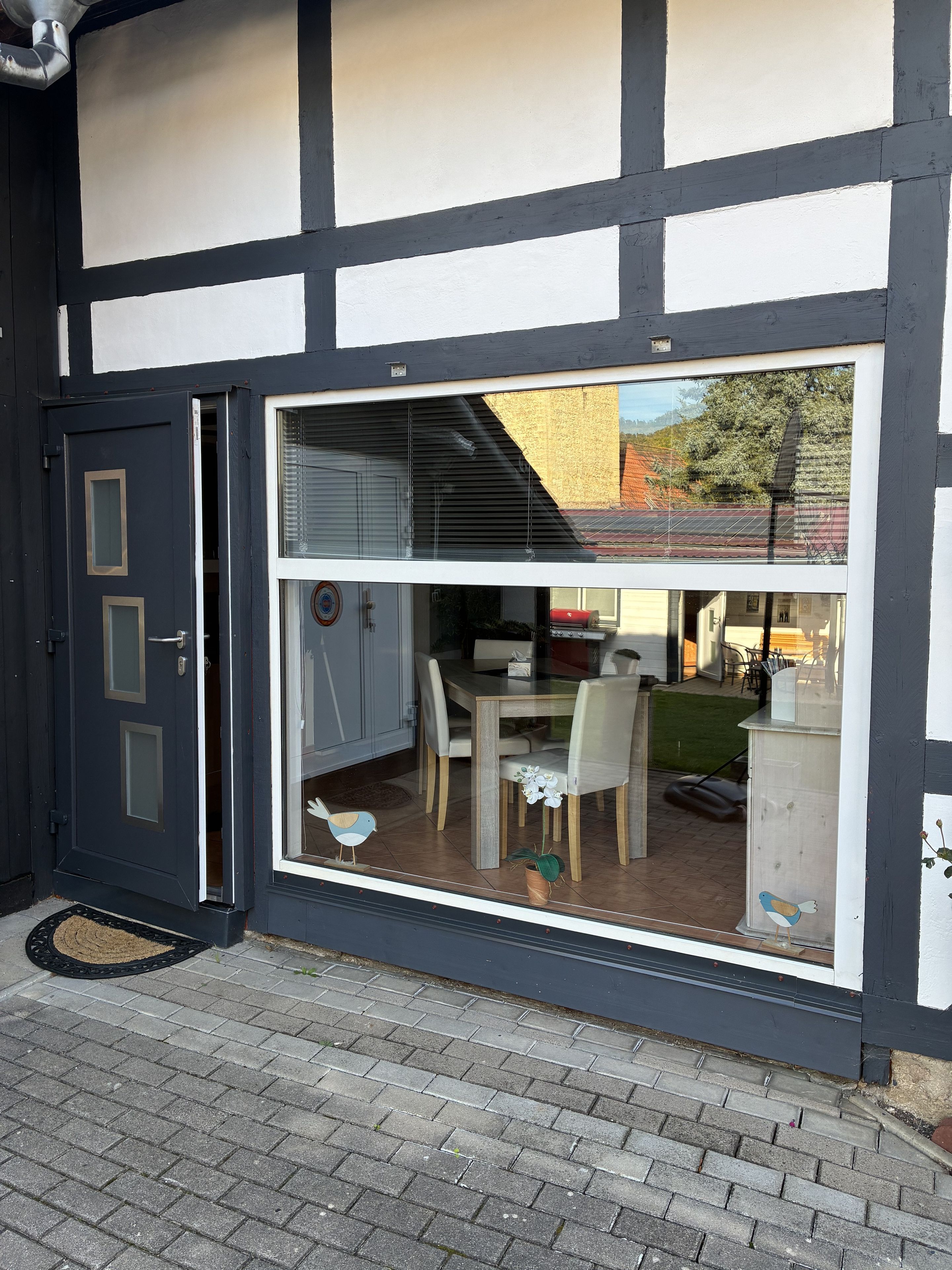 A modern building with a large glass window, a door, and a visible dining area with chairs and a table.
