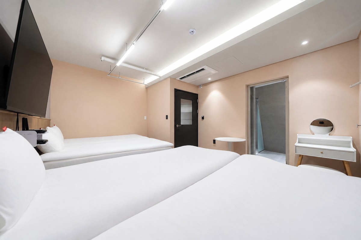 A hotel room with two beds, a TV, a desk, and a bathroom.